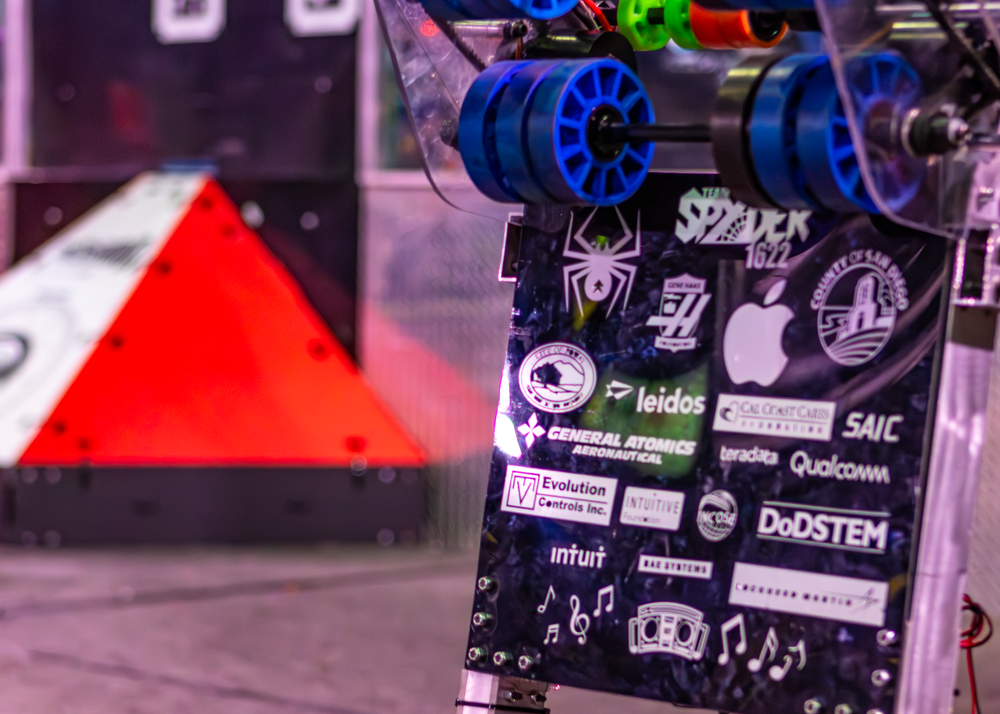 Close-up of robotics team sponsorship stickers and logos on black surface with Spider logo visible.