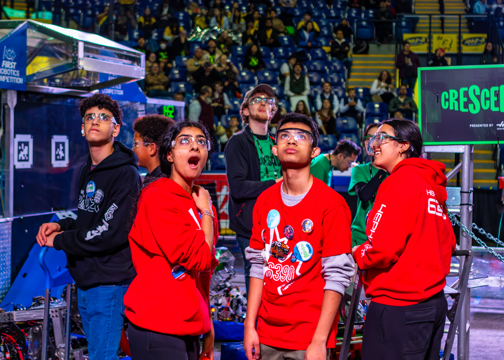 Team members passionately watching their robot compete during a FIRST Robotics match.