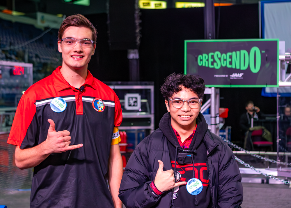 Two competitive gamers pose with medals in front of an illuminated green Crescendo sign at an esports event.