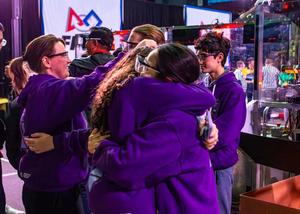 Team members in purple uniforms celebrate together at robotics competition.