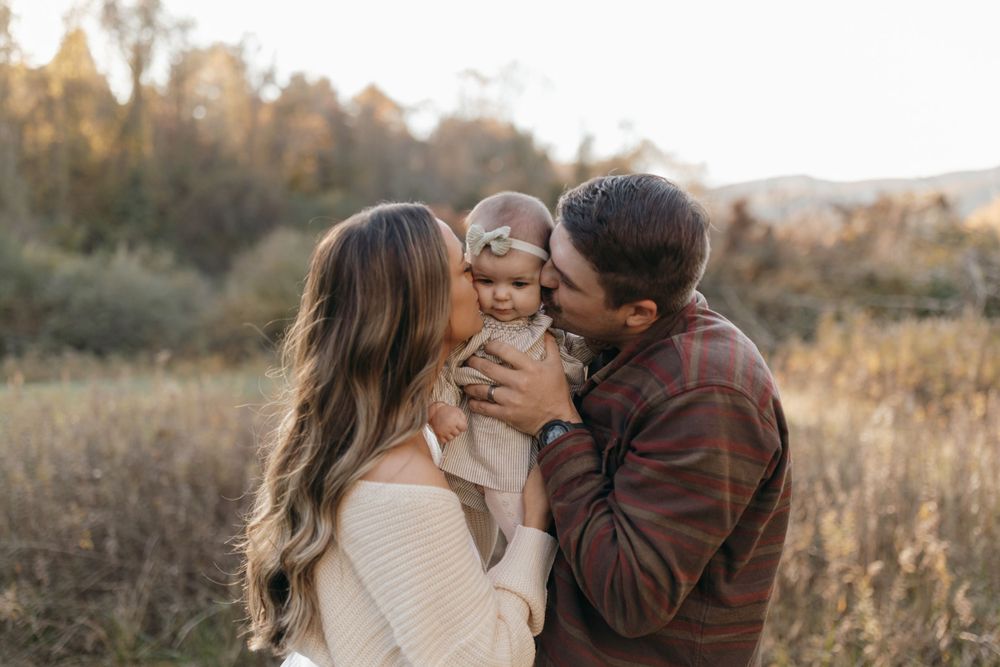 Intimate family portrait showing tender moments between parents and baby in golden sunlight.
