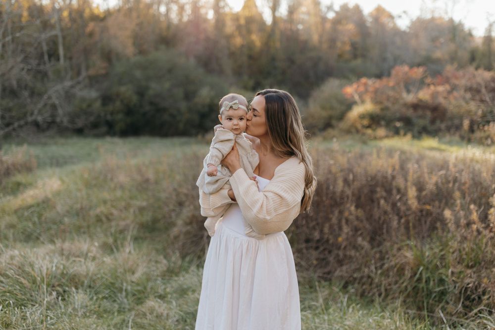 Mother and baby sharing sweet moments in a serene autumn field at sunset.
