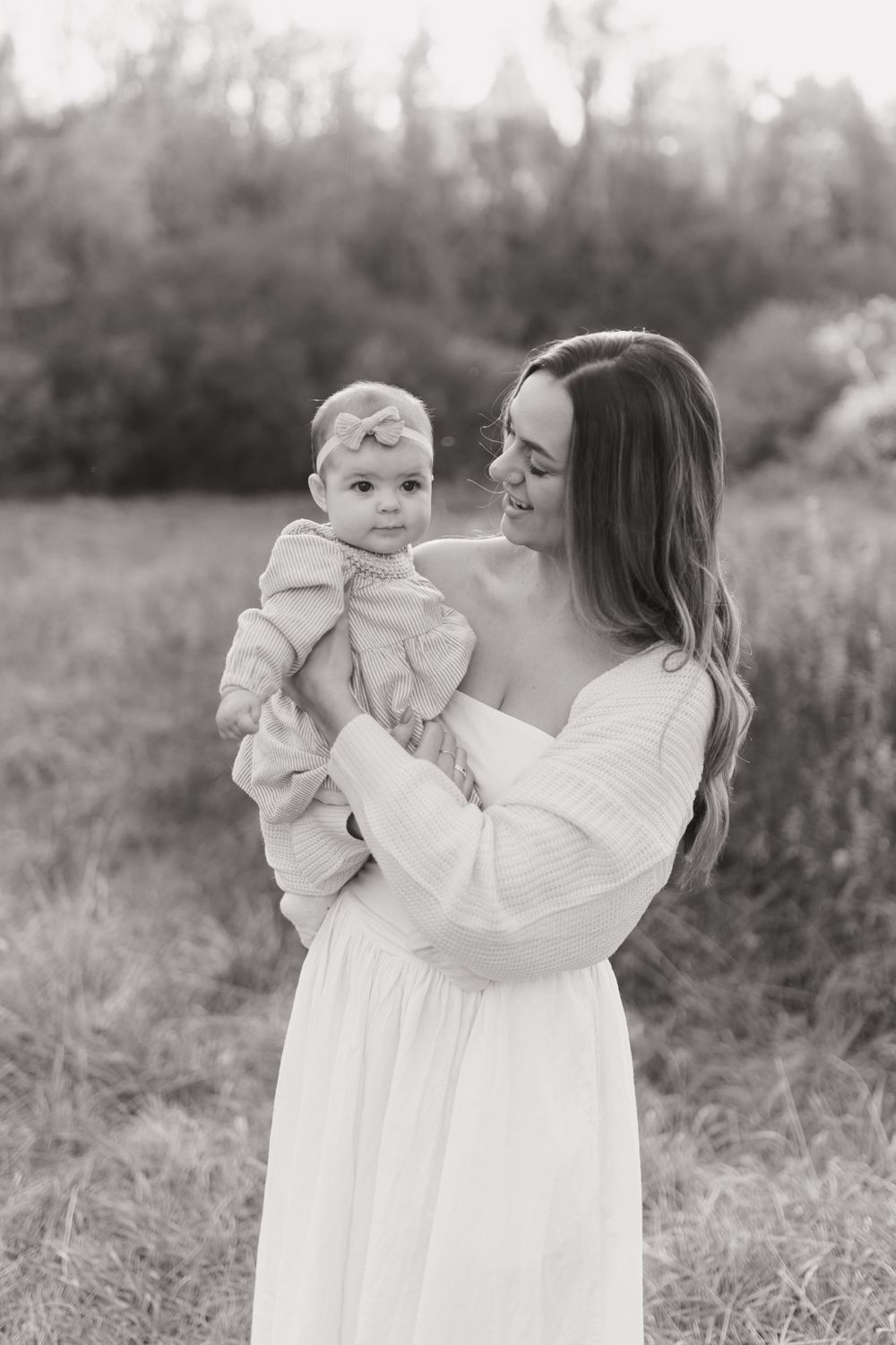 Black and white portrait of mother and baby gazing at each other in a natural outdoor setting.