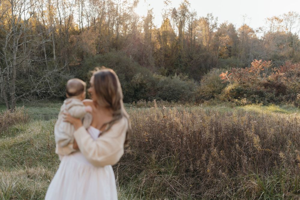 Mother holding baby while standing in a misty autumn field at dusk.