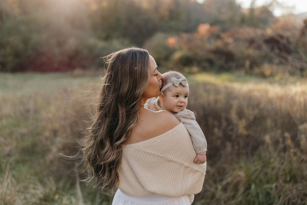 Mother and baby portrait taken during golden hour in a rustic autumn field.