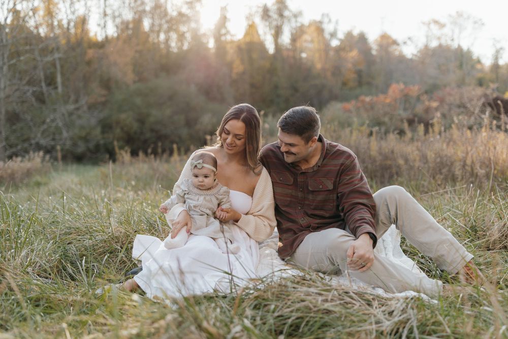 Family sits together on grass during a warm autumn sunset photoshoot.