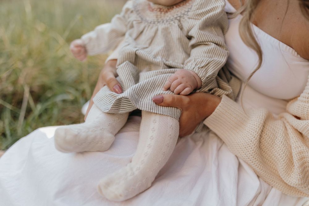 Close-up detail of a baby wearing a ruffled cream dress and white socks sitting in someone's lap.
