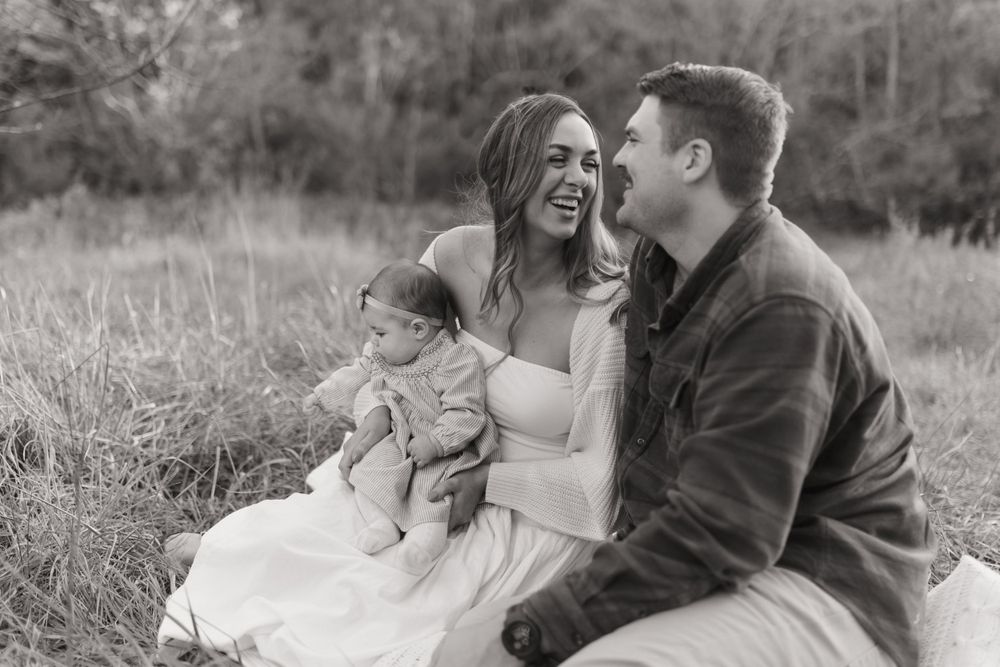 A candid black and white family moment captured during an outdoor photoshoot in a grassy field.