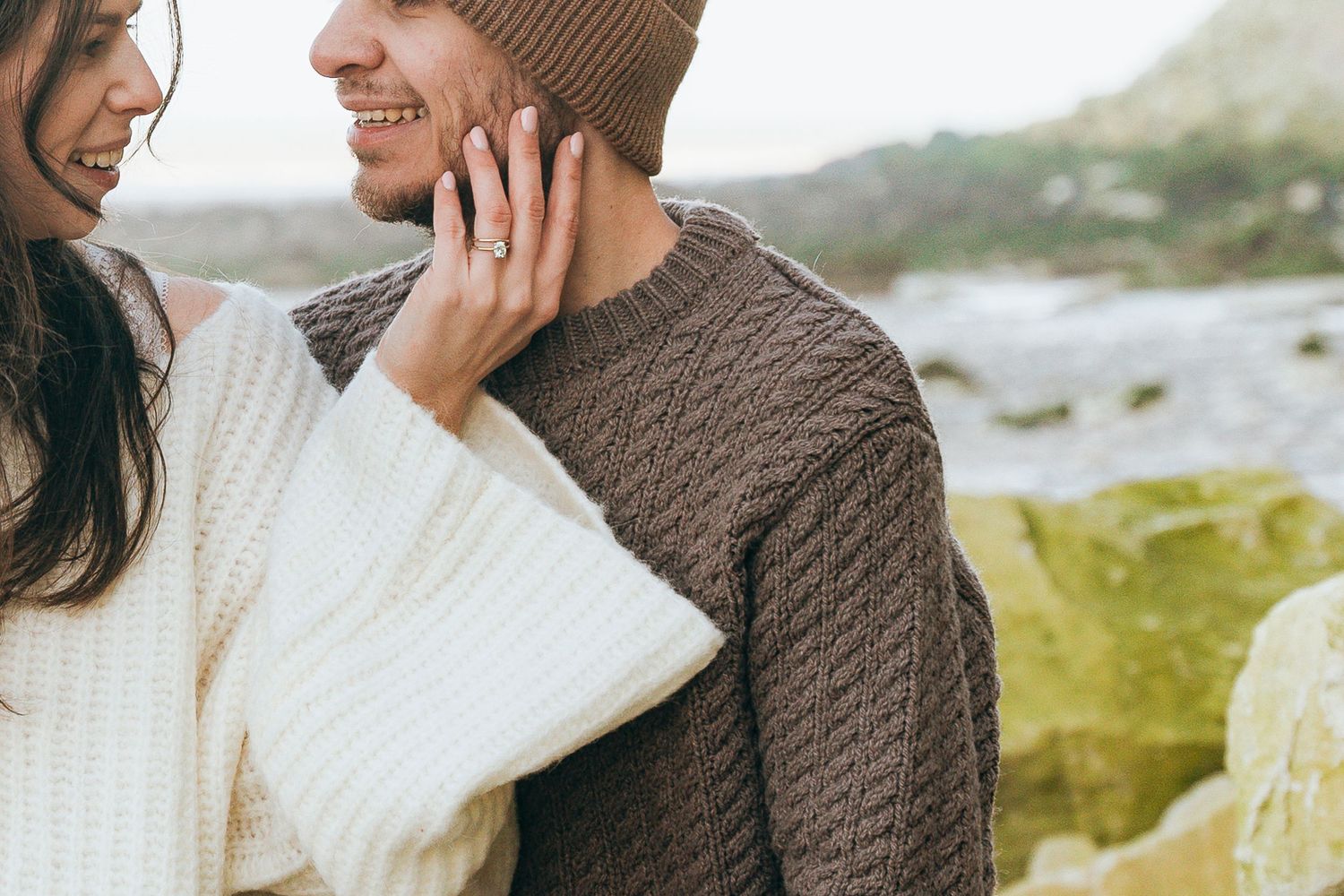 Close-up of a couple in cozy sweaters sharing an intimate moment outdoors near a coastal landscape.