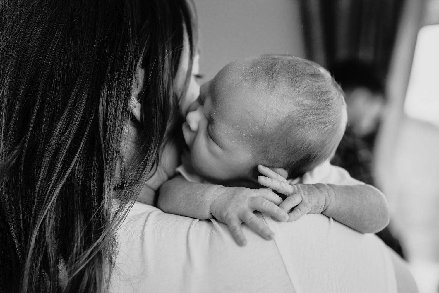 A tender black and white moment captured as a baby rests on a shoulder, reaching out with their tiny hand.