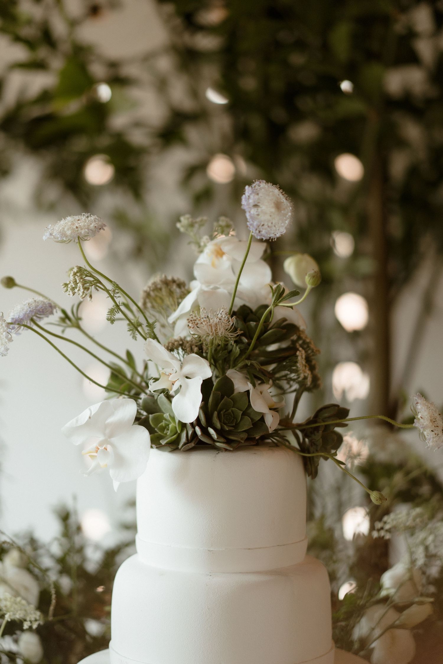 White tiered wedding cake decorated with delicate white flowers and greenery.