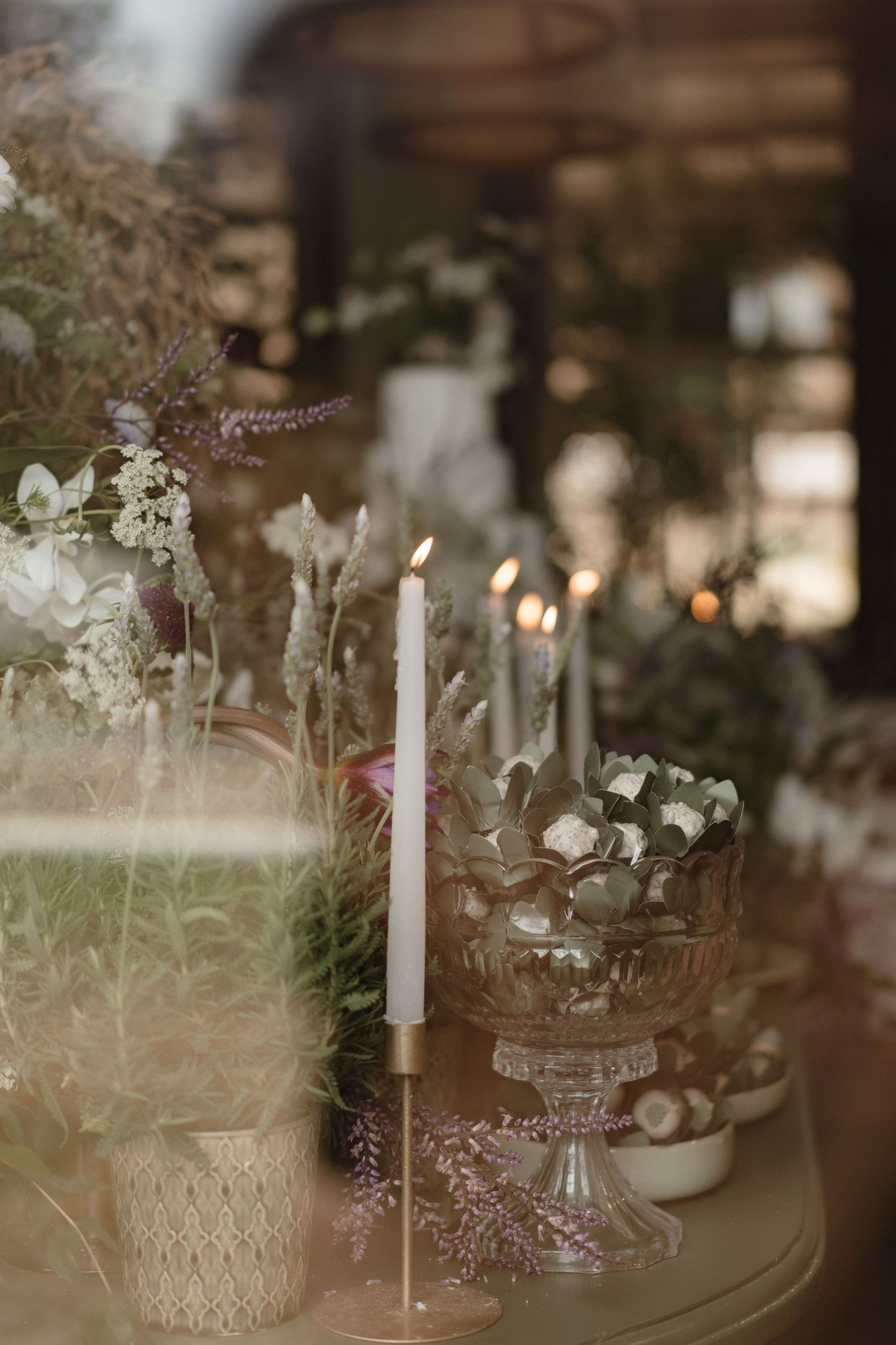Romantic table setting with white candles and floral arrangements in vintage glass containers.