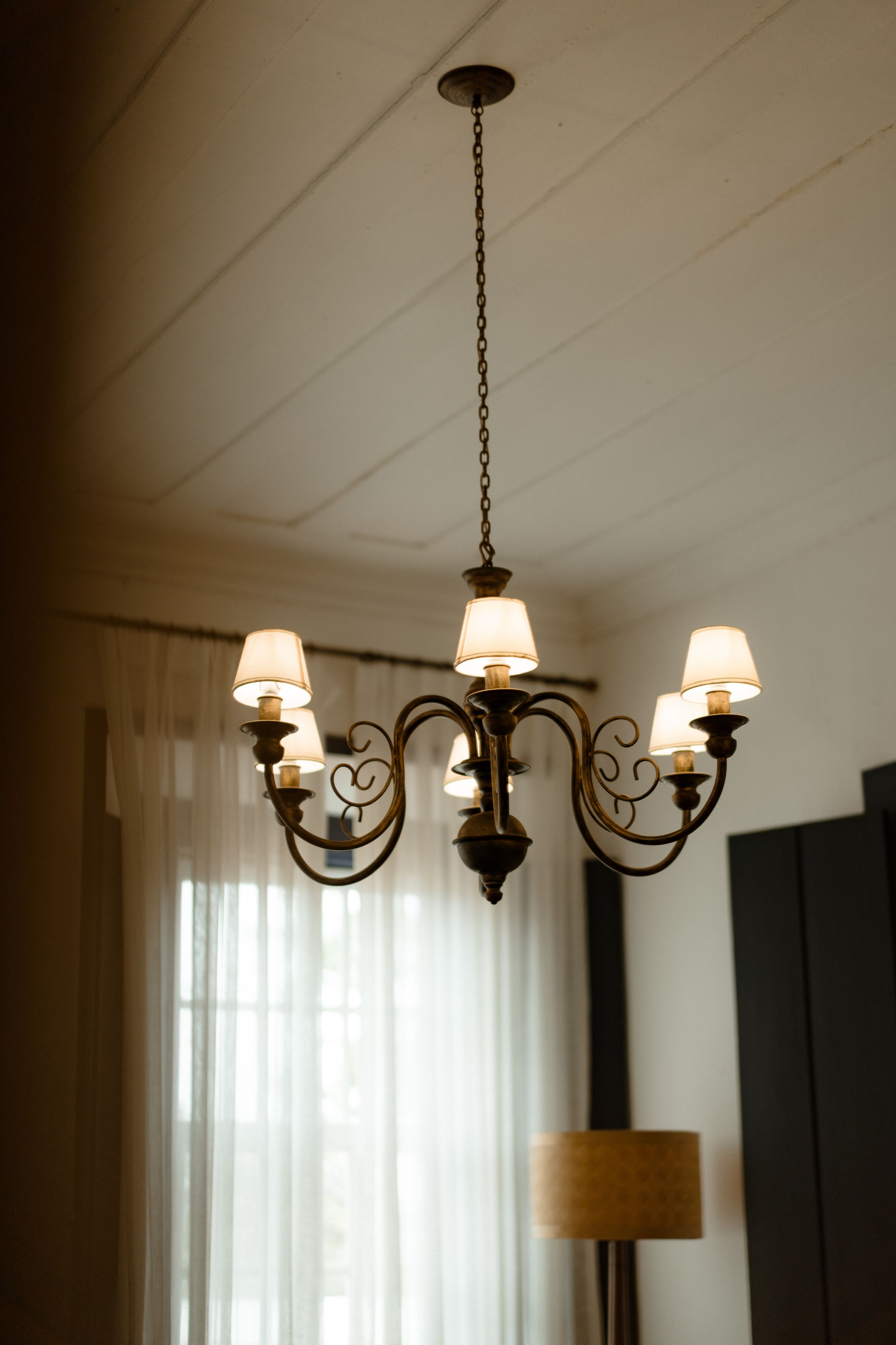 An elegant wrought iron chandelier with white shades hangs from a white ceiling in a classic interior.