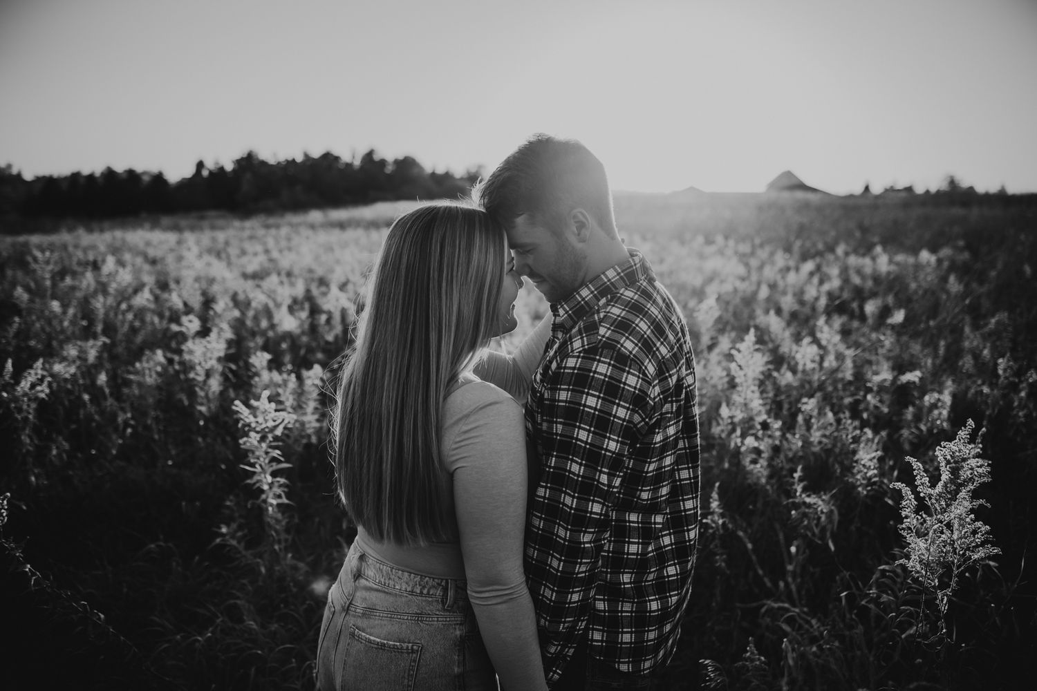 Black and white photo of couple embracing in a field at sunset.