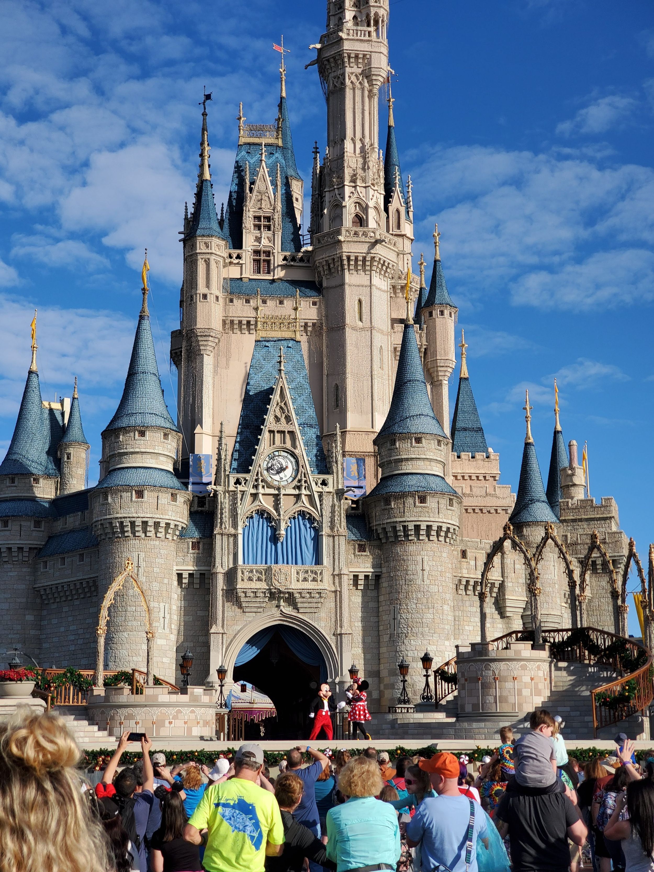 Cinderella Castle at Walt Disney World's Magic Kingdom towers over crowds of visitors under a bright blue sky.