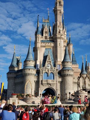 Crowds gather in front of Cinderella Castle at Walt Disney World's Magic Kingdom on a sunny day with blue skies.