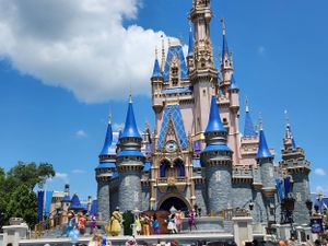 Cinderella Castle at Disney World's Magic Kingdom stands majestically against a blue sky with white fluffy clouds.