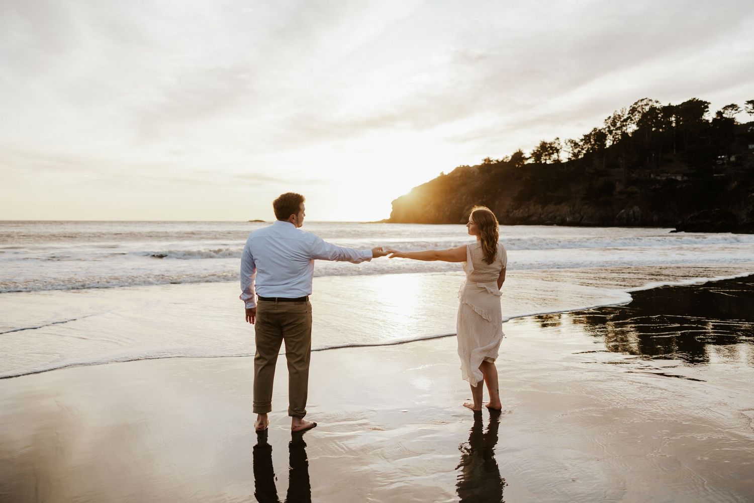 romantic photo of couple standing on muir beach at sunset while reaching hands towards each other - san francisco bay area engagement photos