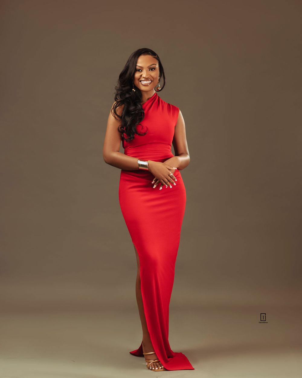 Elegant studio portrait in a flowing red evening gown against brown background.