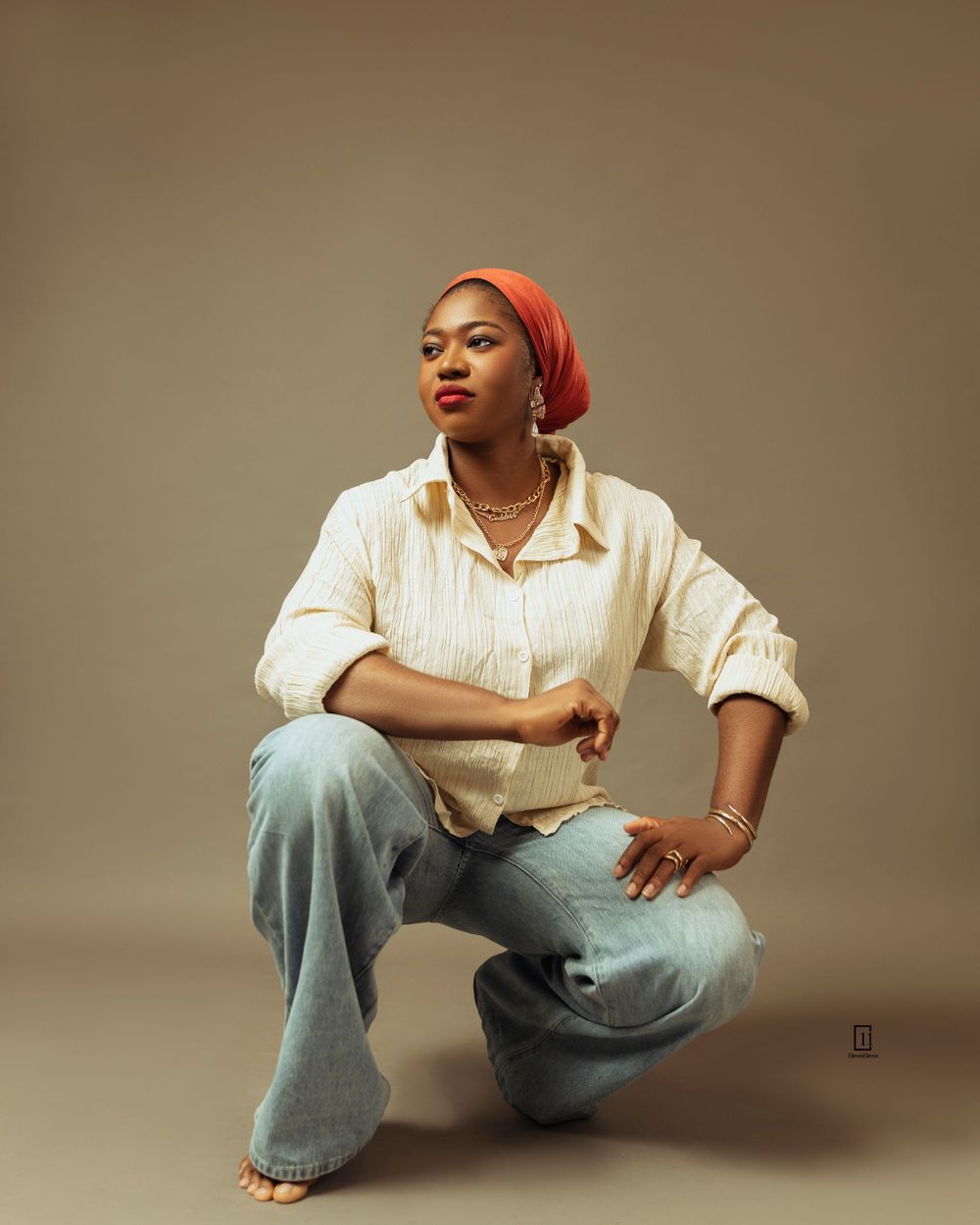 Artistic portrait in cream blouse, jeans and red headwrap against neutral studio background.