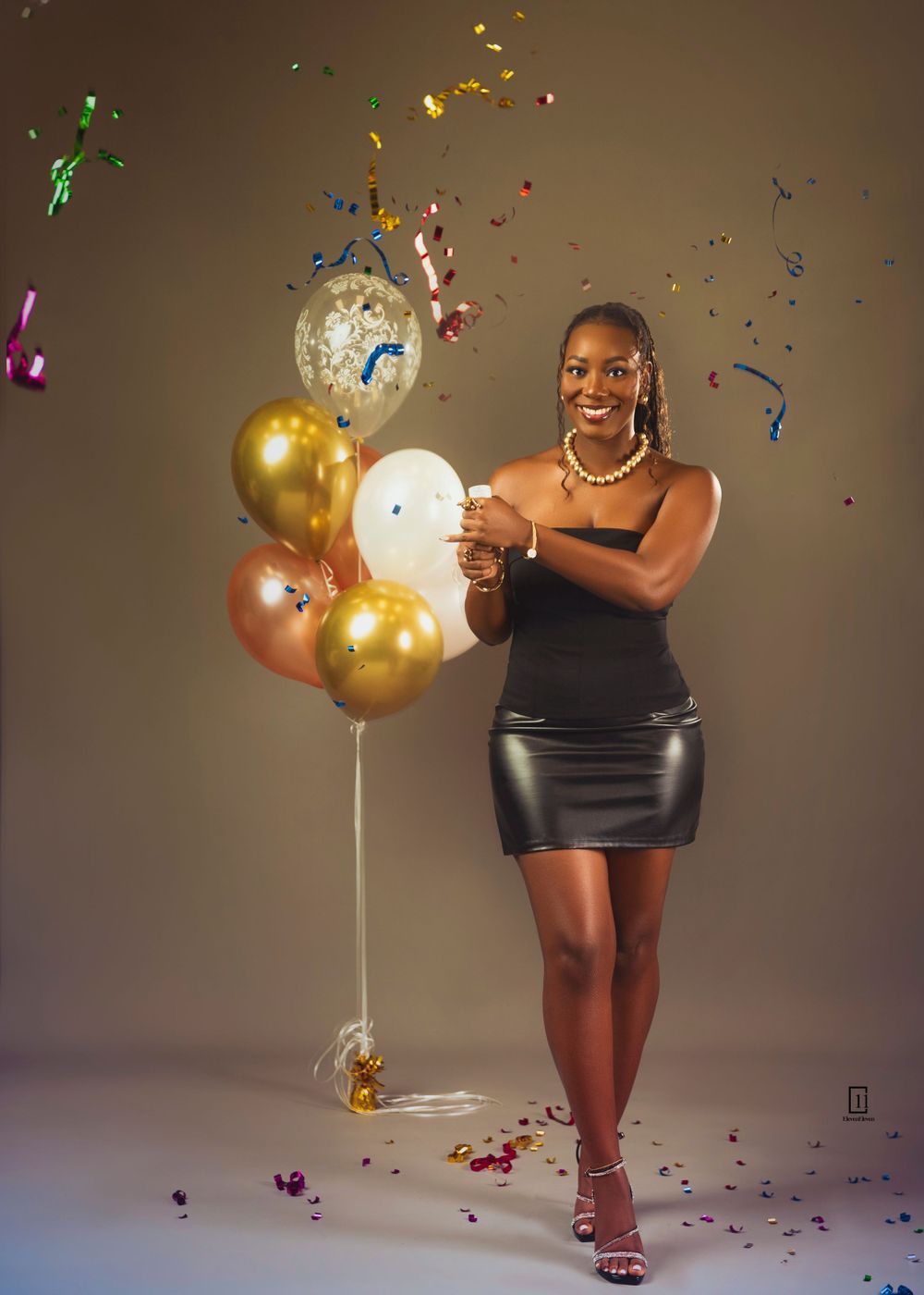 Celebration photo shoot with gold and silver balloons and confetti against brown backdrop.