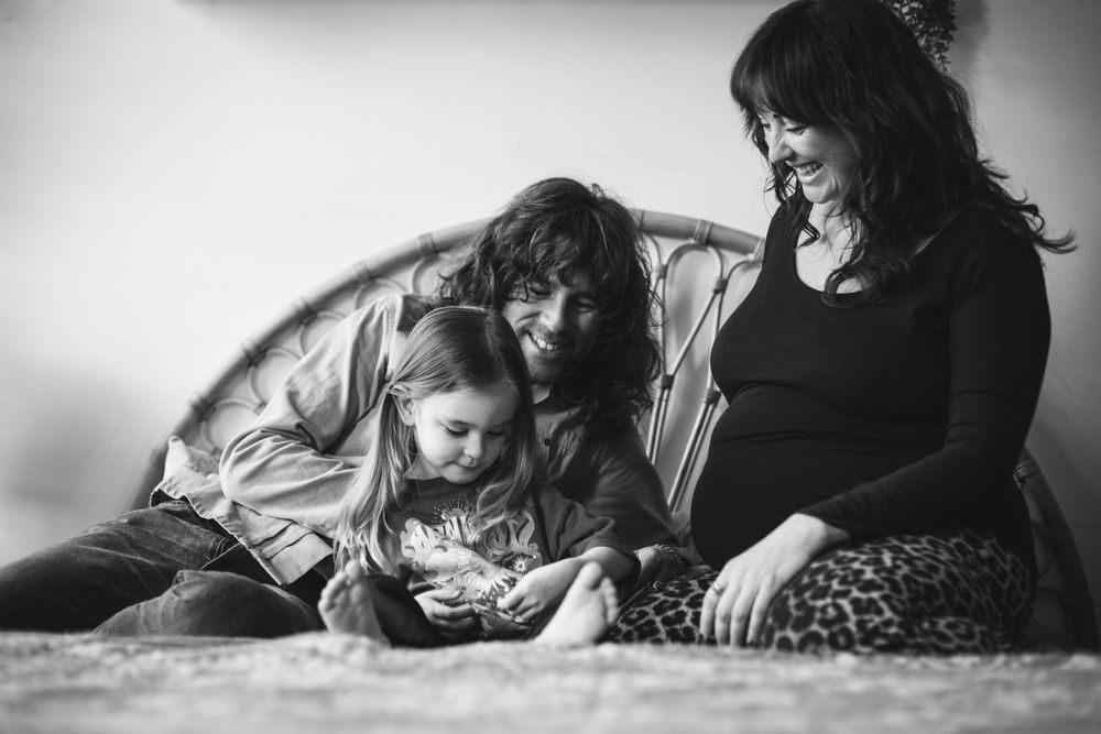 A black and white photograph of a family looking at a mobile device together while relaxing on a couch.