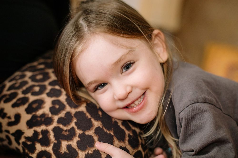 A joyful child laying on a leopard print pillow while smiling at the camera.