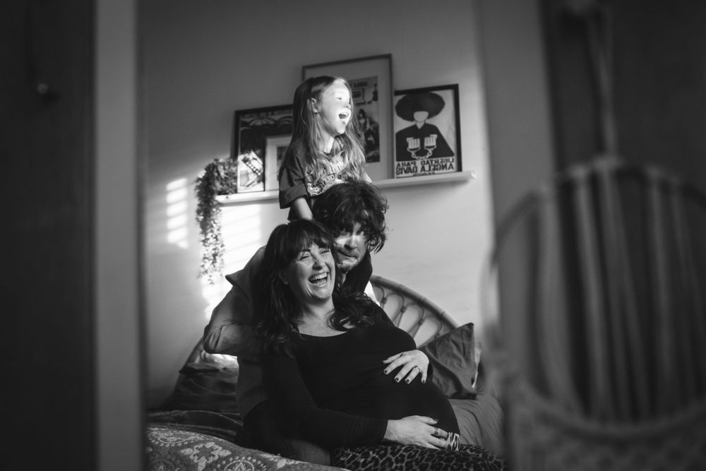 A black and white portrait shows two people lounging together on a couch in a domestic interior setting.