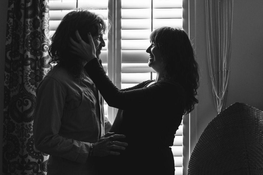 A romantic black and white silhouette shows a couple in an intimate moment by a window with plantation shutters.