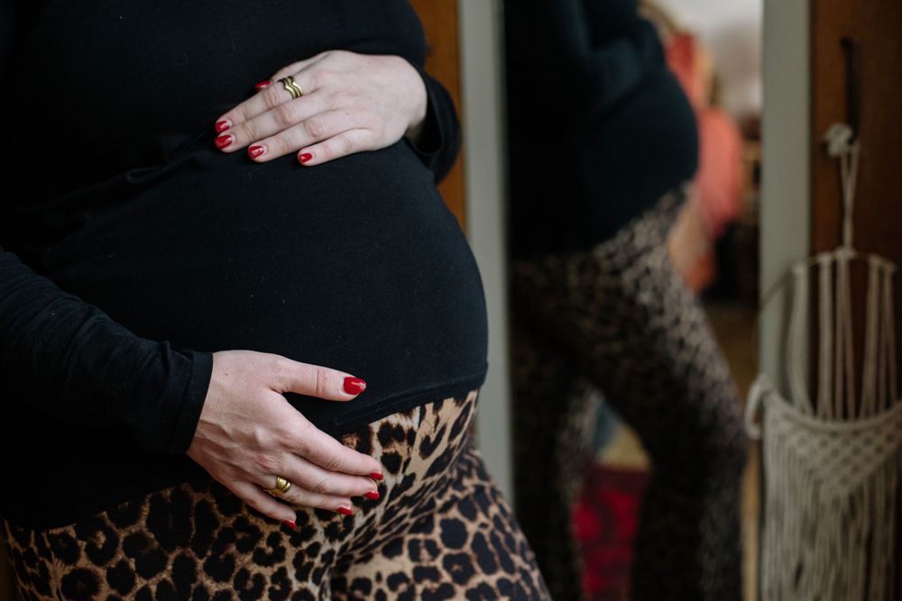 Hands rest tenderly on a pregnant belly wearing a leopard print dress during a maternity photo shoot.