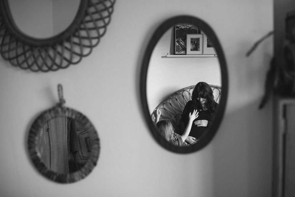 Black and white reflection in a round mirror showing someone taking a photo amidst circular wall decor.