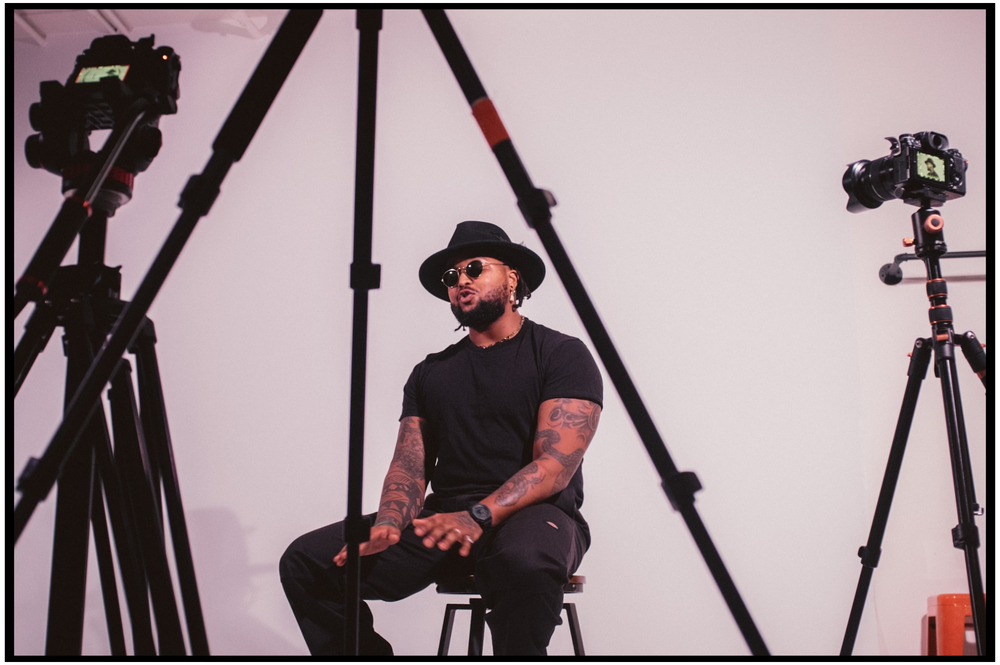 Musician sits on stool between camera equipment during photo session. Portland music photographer