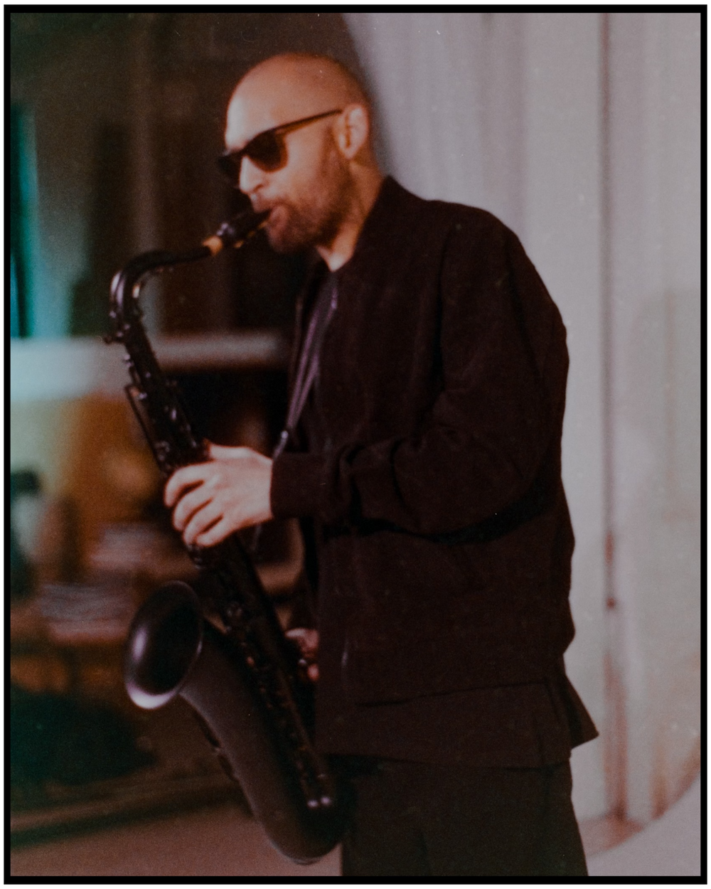 Saxophone player in dark jacket performs in atmospheric lighting. Portland music photographer