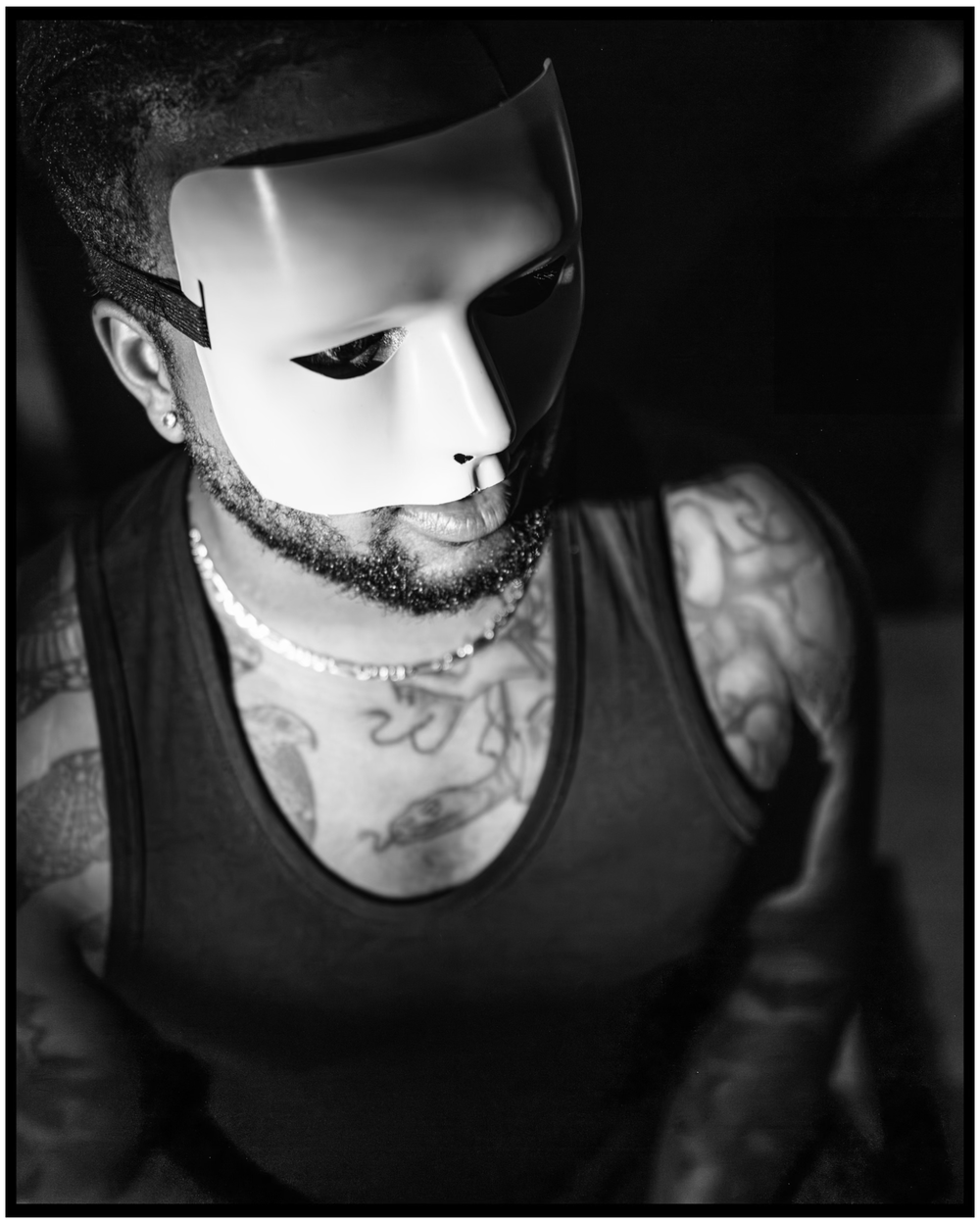 Artistic black and white photo of someone wearing a white mask and tank top showing tattoos. Portland music photographer