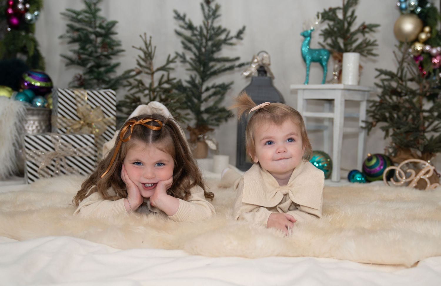 Children lying on white fluffy carpet near decorated Christmas trees.