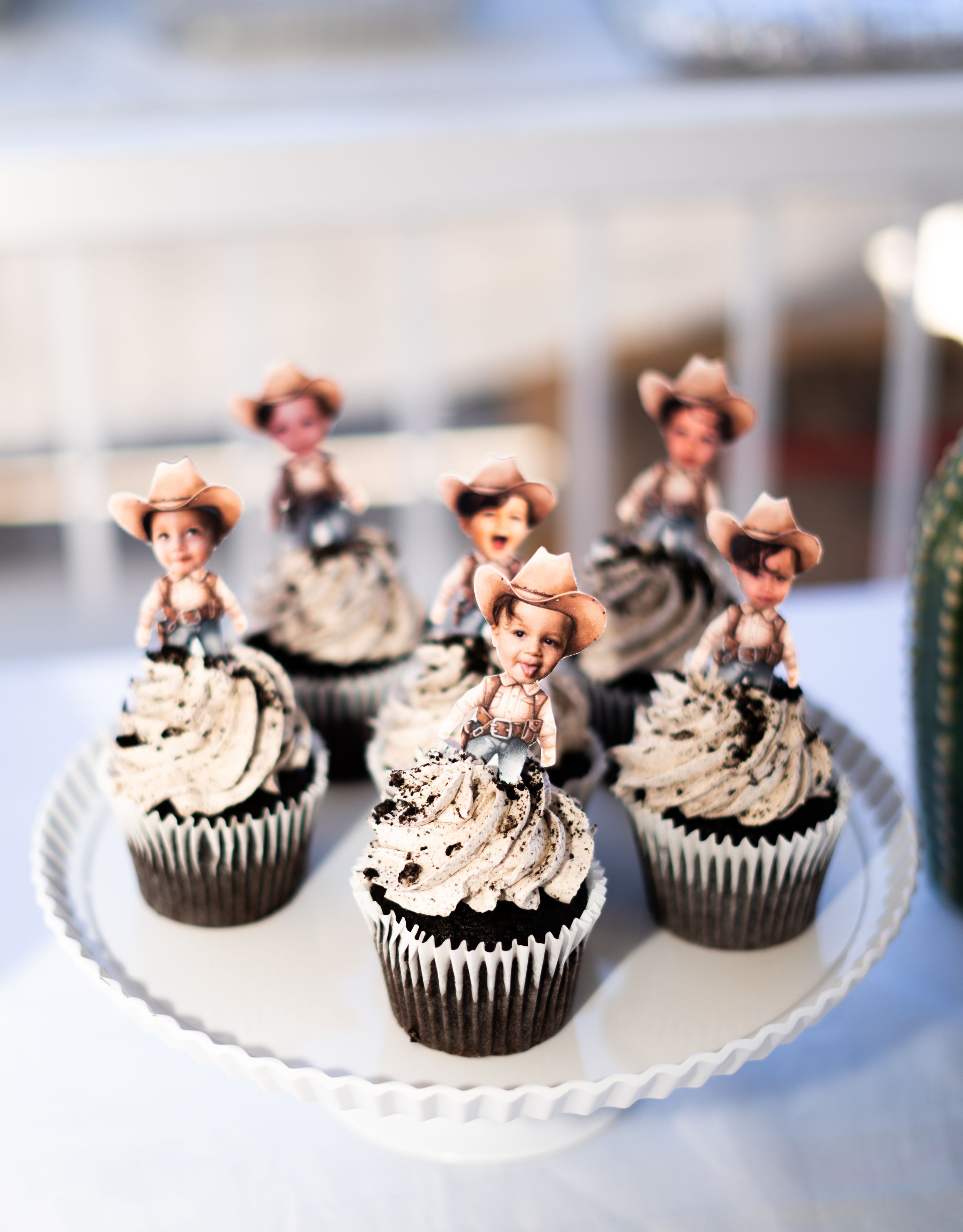 Chocolate cupcakes with swirled frosting topped with pink decorative elements on white cake stand.