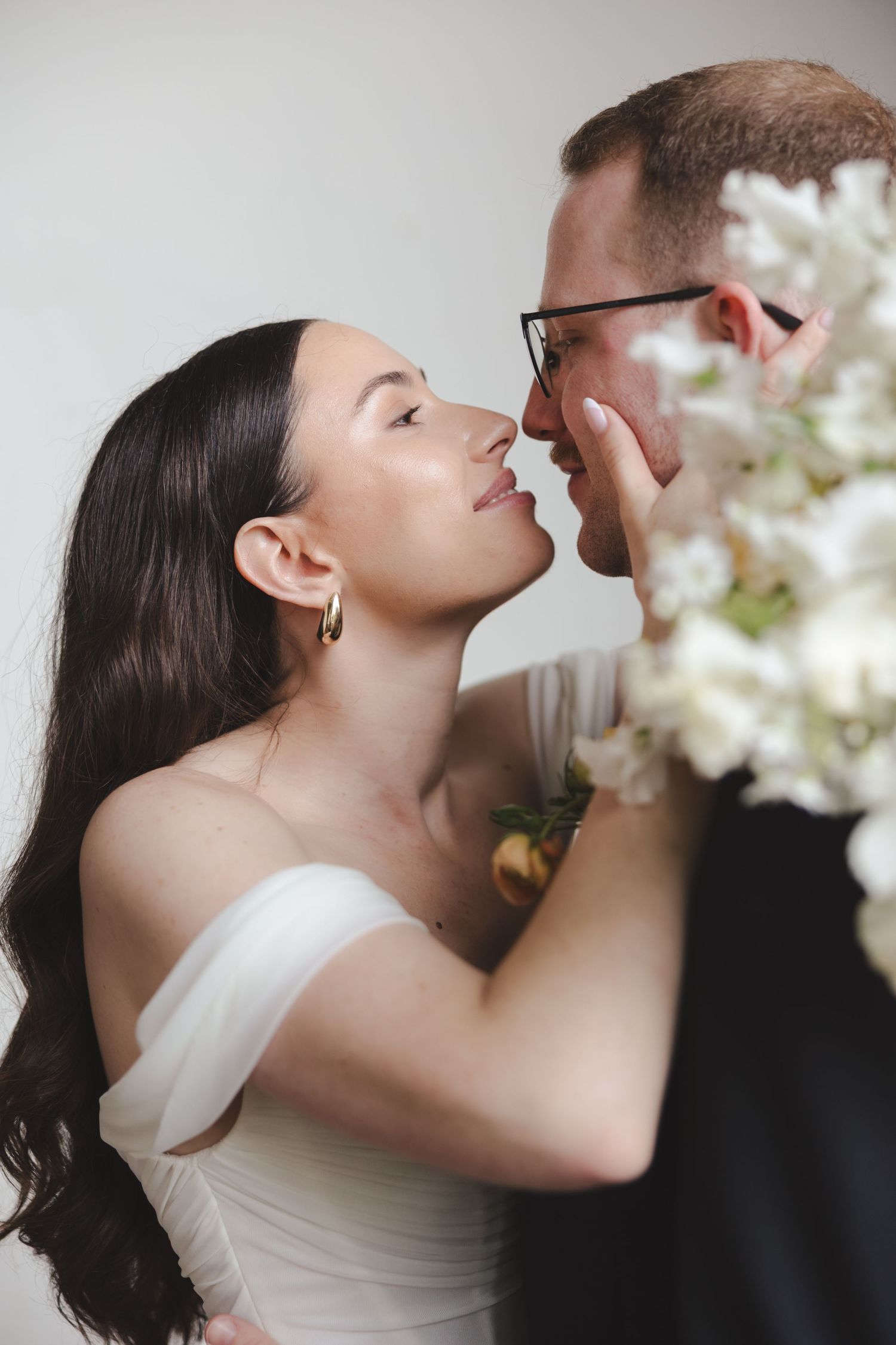 A romantic wedding moment captured outdoors with a white rose bouquet and flowing veil on a grassy lawn.