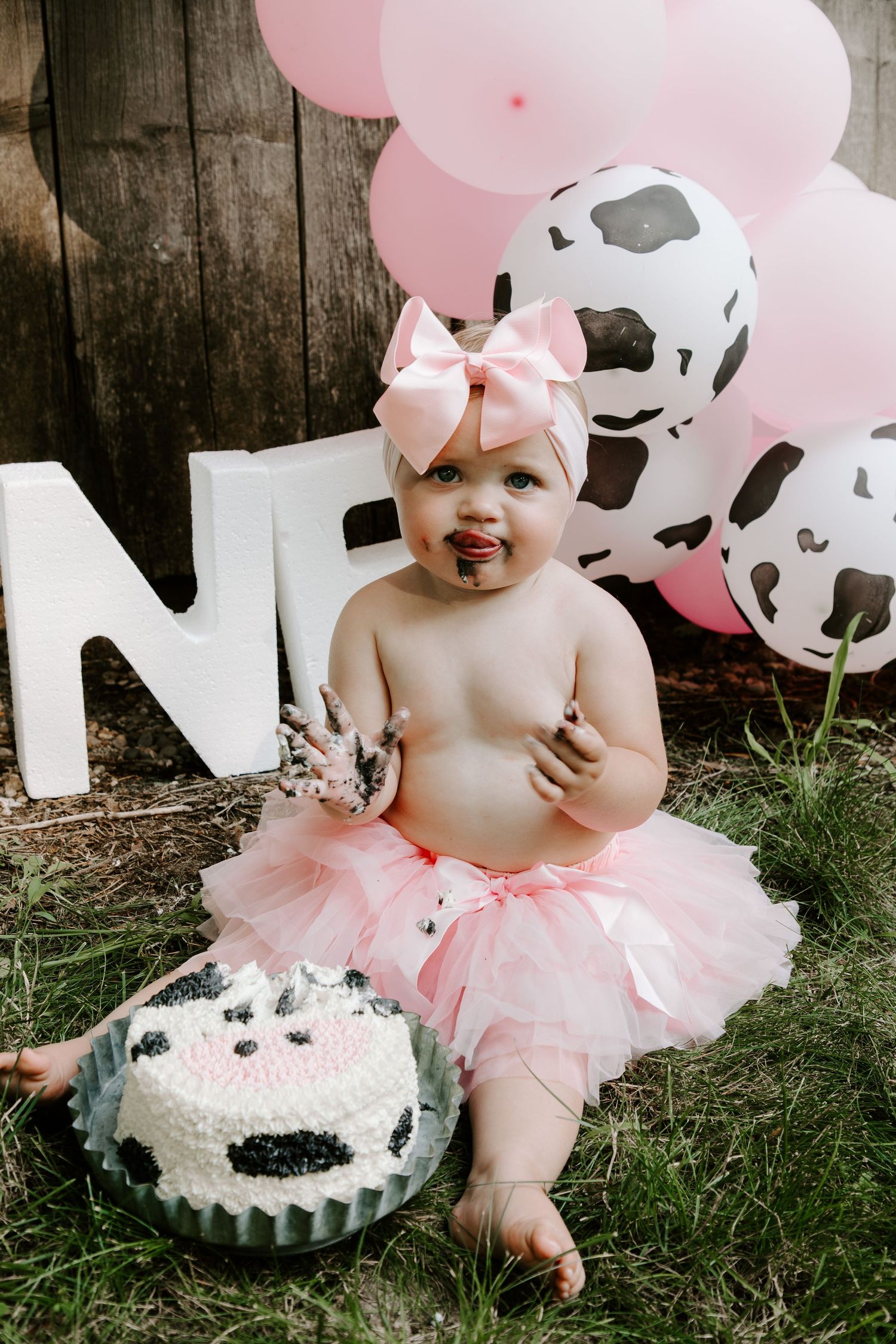 Pink cow print party setup with balloons, tutu, and matching smash cake for a first birthday celebration.