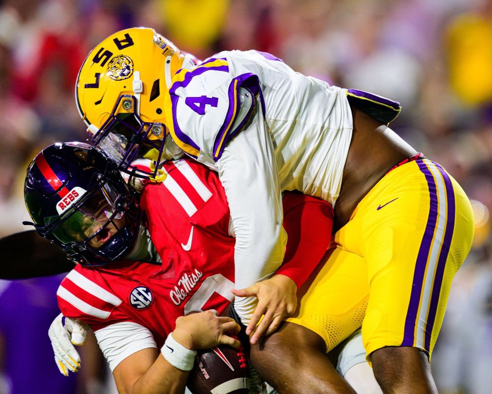 Football players from LSU and Ole Miss collide in aggressive tackle during game.