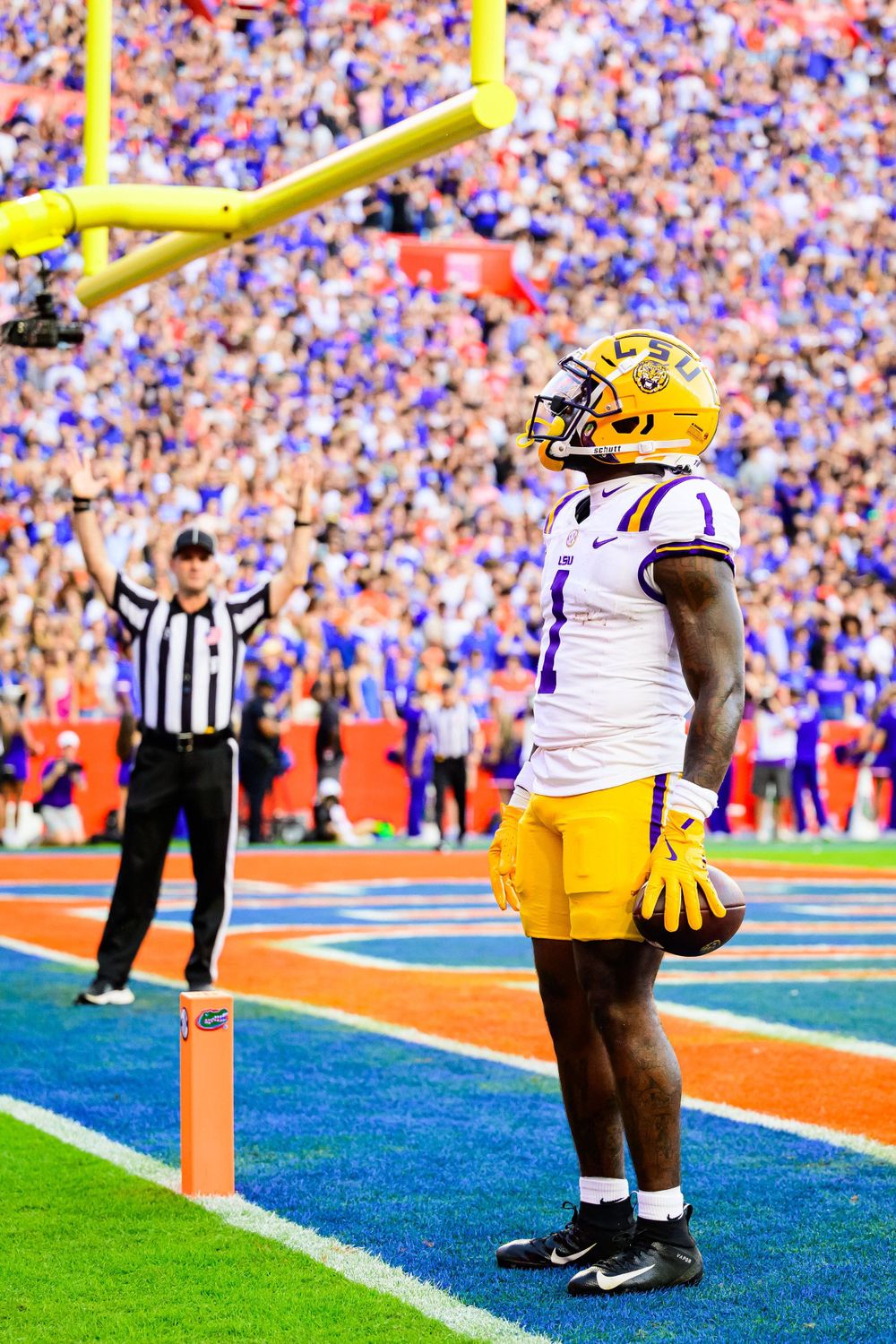 Football player in LSU uniform standing in endzone with yellow goal post and crowd in background.