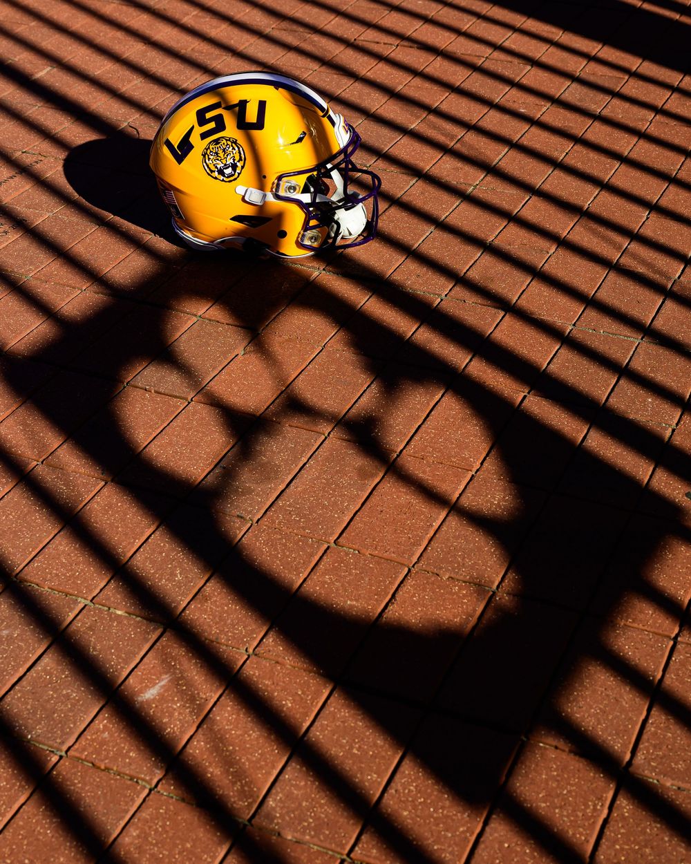 Yellow football helmet casting dramatic shadows on a brown tiled surface in dramatic lighting.