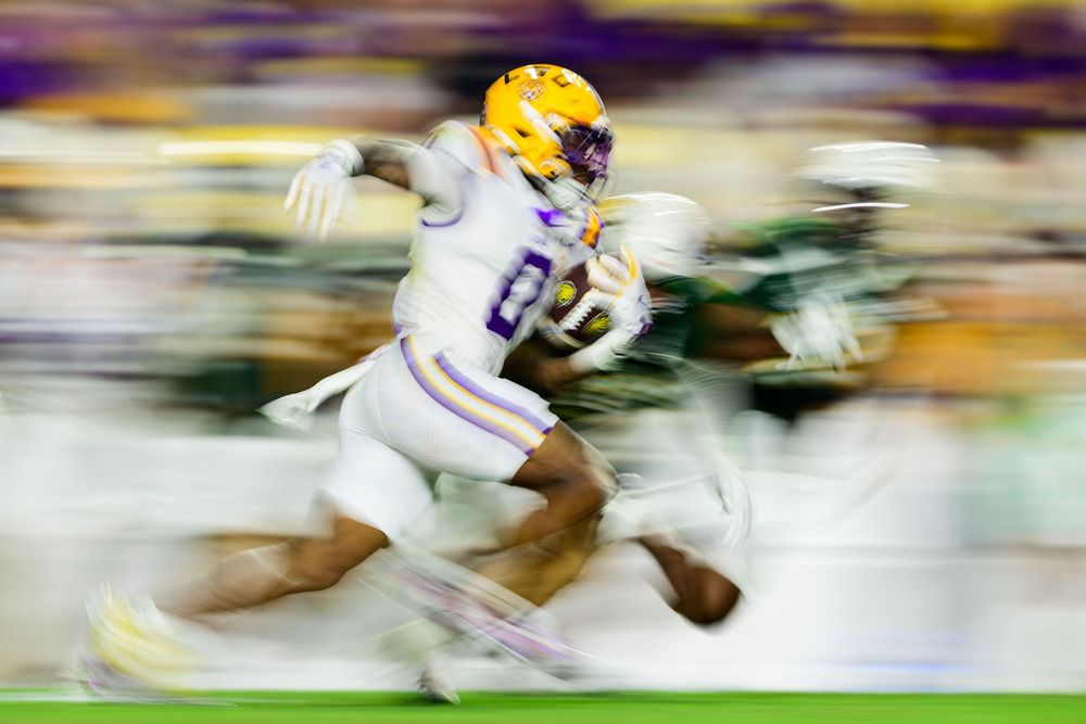 A football player in white and purple uniform runs with the ball during a fast-paced game action sequence.