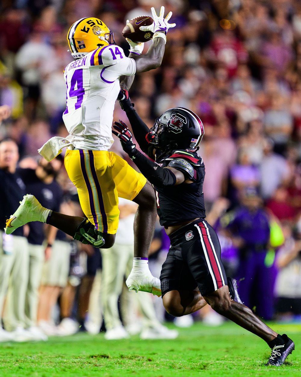 Football players from LSU and South Carolina collide during an intense tackle play on the field.