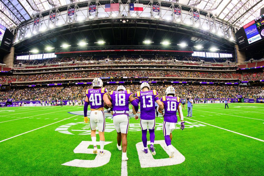 Vikings players walking onto field at indoor stadium showing 50-yard line marker.