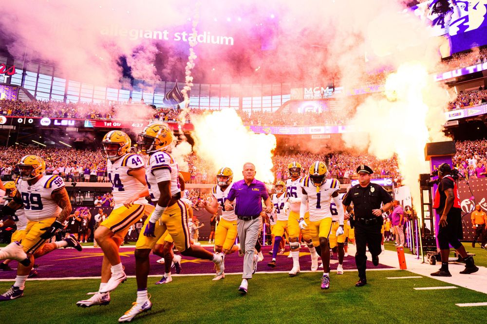 Football team runs onto field through purple smoke and pyrotechnics display.