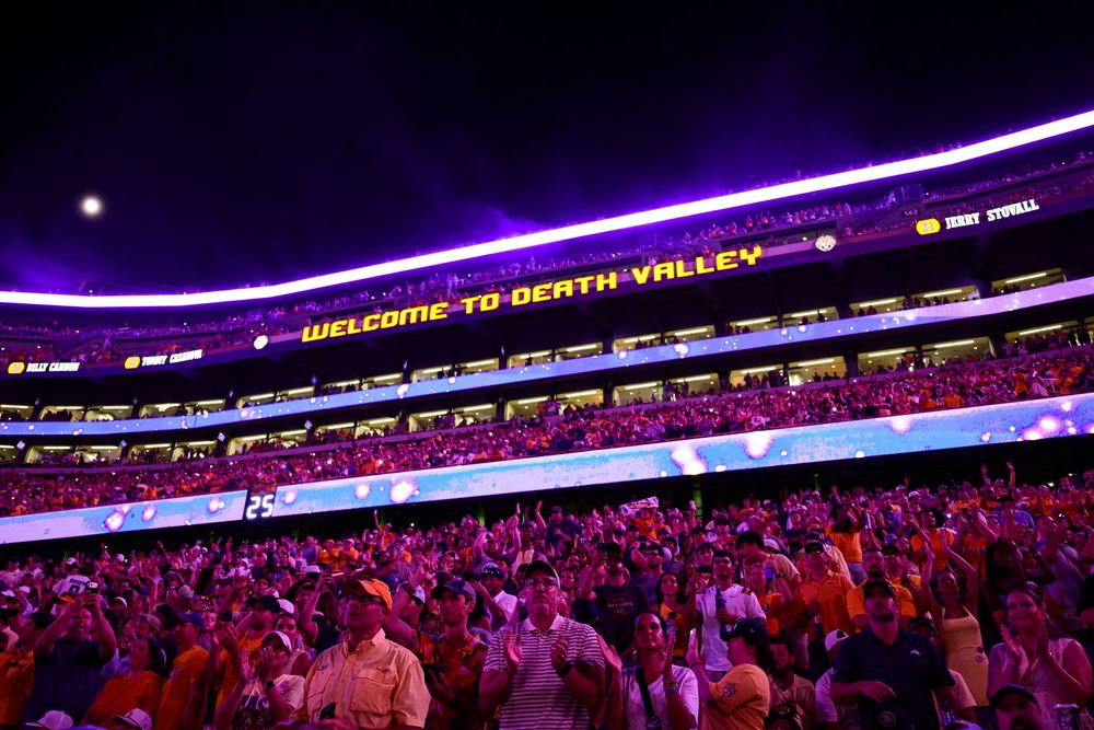 Fans in orange fill a packed stadium at night under a glowing purple Welcome to Death Valley sign on the upper deck.
