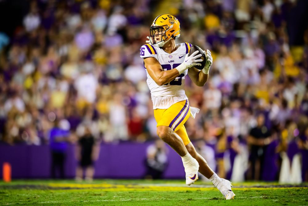LSU football player in yellow jersey catches ball during night game.
