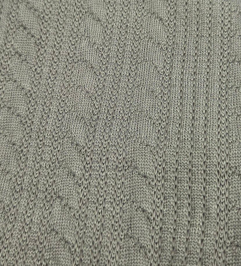 Close-up texture of gray knitted or woven fabric with diamond and cable patterns showing detailed stitch work.