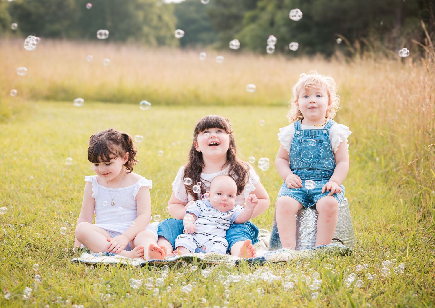 Children sitting together in a sunny meadow with bubbles floating through the air.