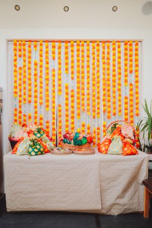 Orange and white marigold garland backdrop with colorful decorative pillows on a table.